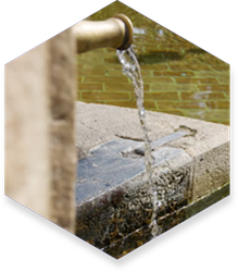 Water pouring from a brass faucet into a stone basin. Brick wall background.