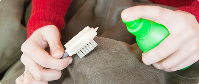 Person spraying a green bottle onto a fabric and holding a brush.
