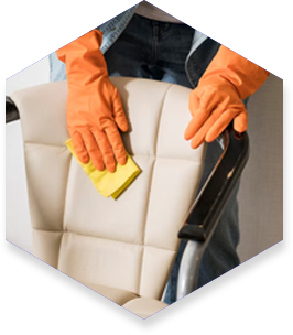 Person in orange gloves wiping down a white office chair with a yellow cloth.