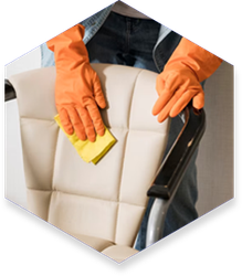 Person in orange gloves wiping down a white office chair with a yellow cloth.