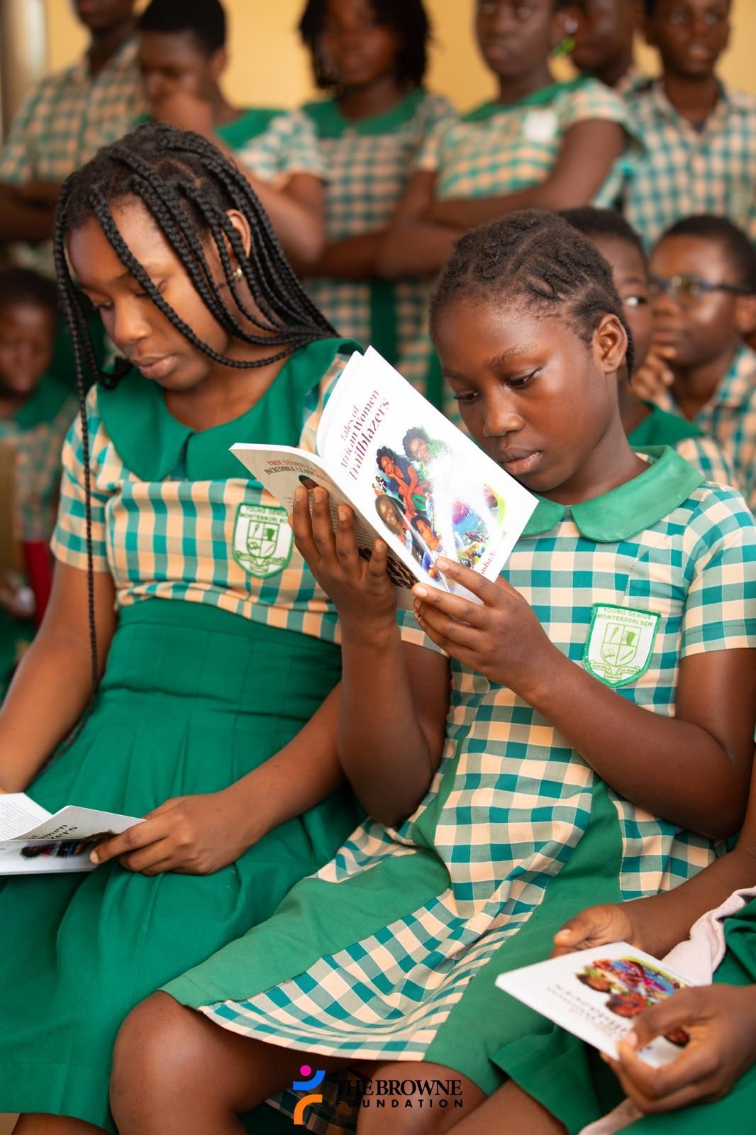 Two girls in school uniforms reading books in a classroom.