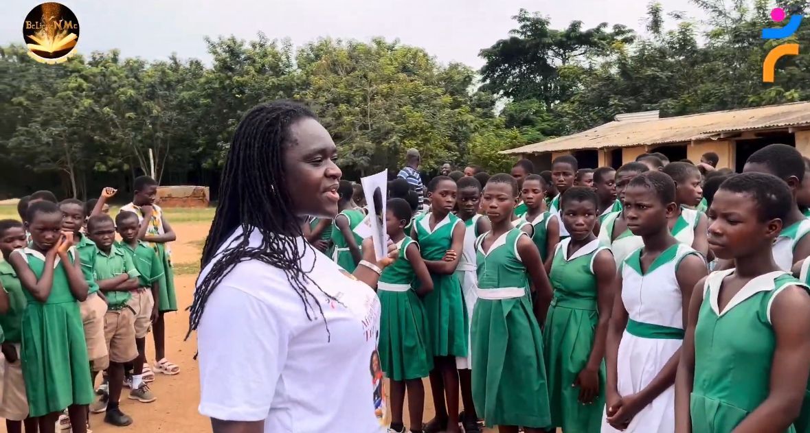 Woman speaks to school children in green uniforms outdoors.