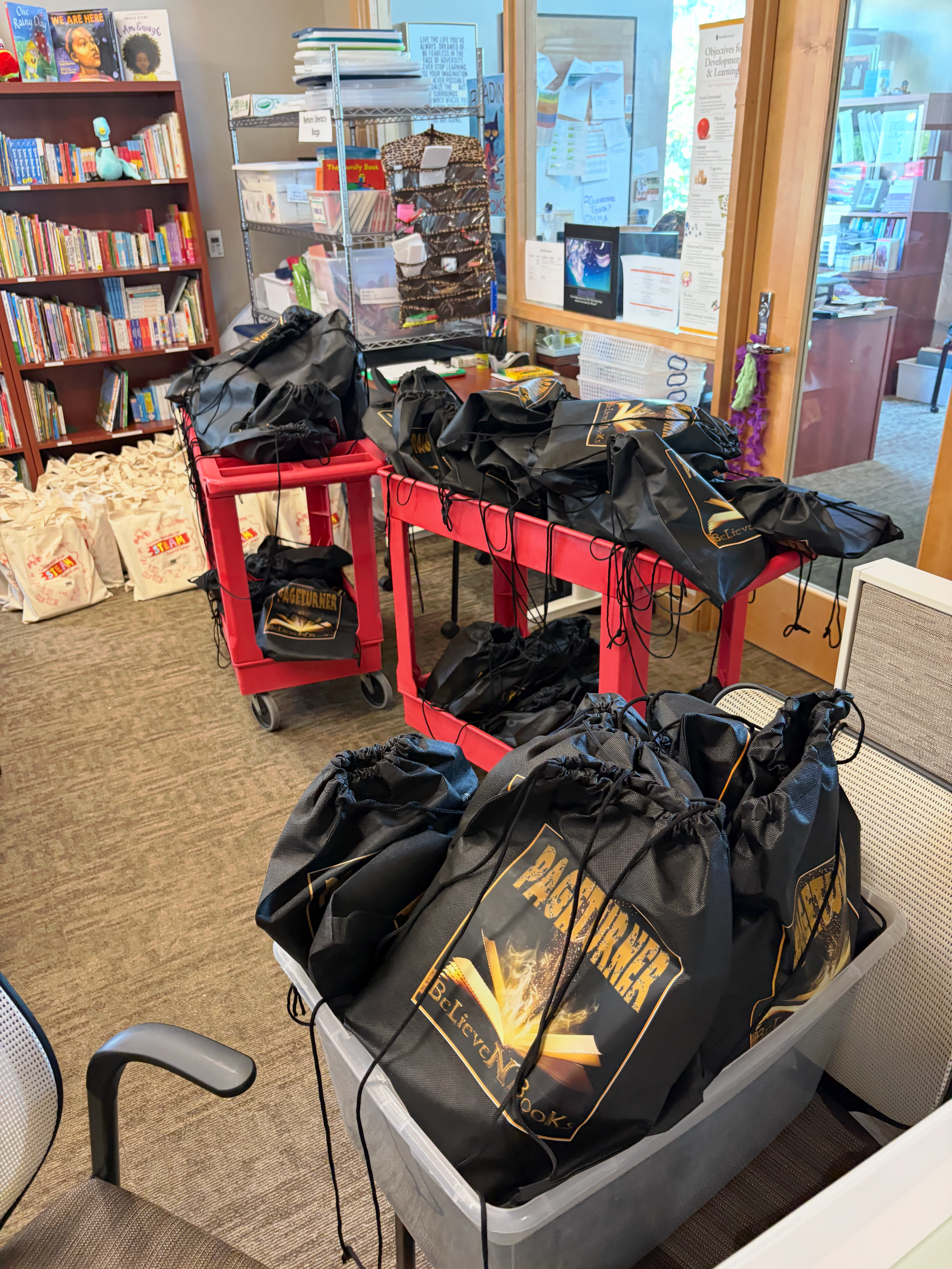 Black bags with drawstring closures on a red cart and in a bin. Library setting.
