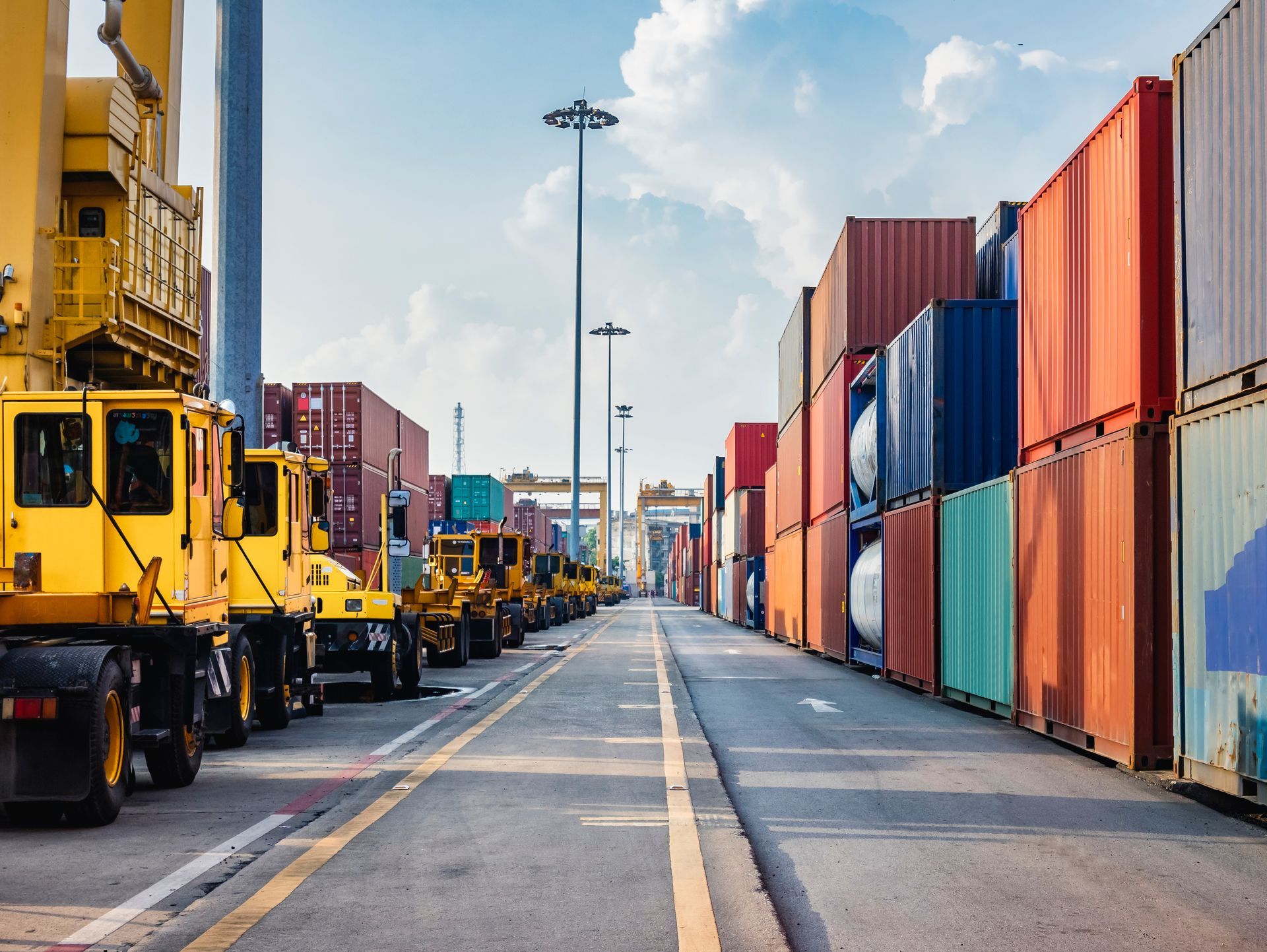 Shipping containers stacked at a port, yellow machinery, blue sky.