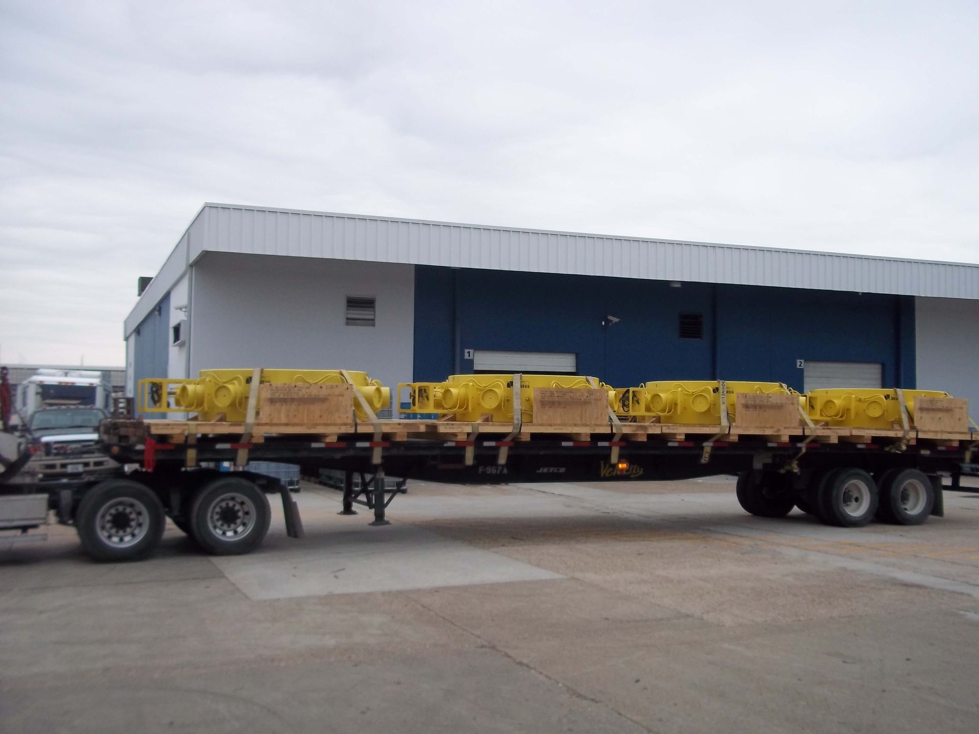 A flatbed trailer loaded with yellow crates, parked near a blue and white building.