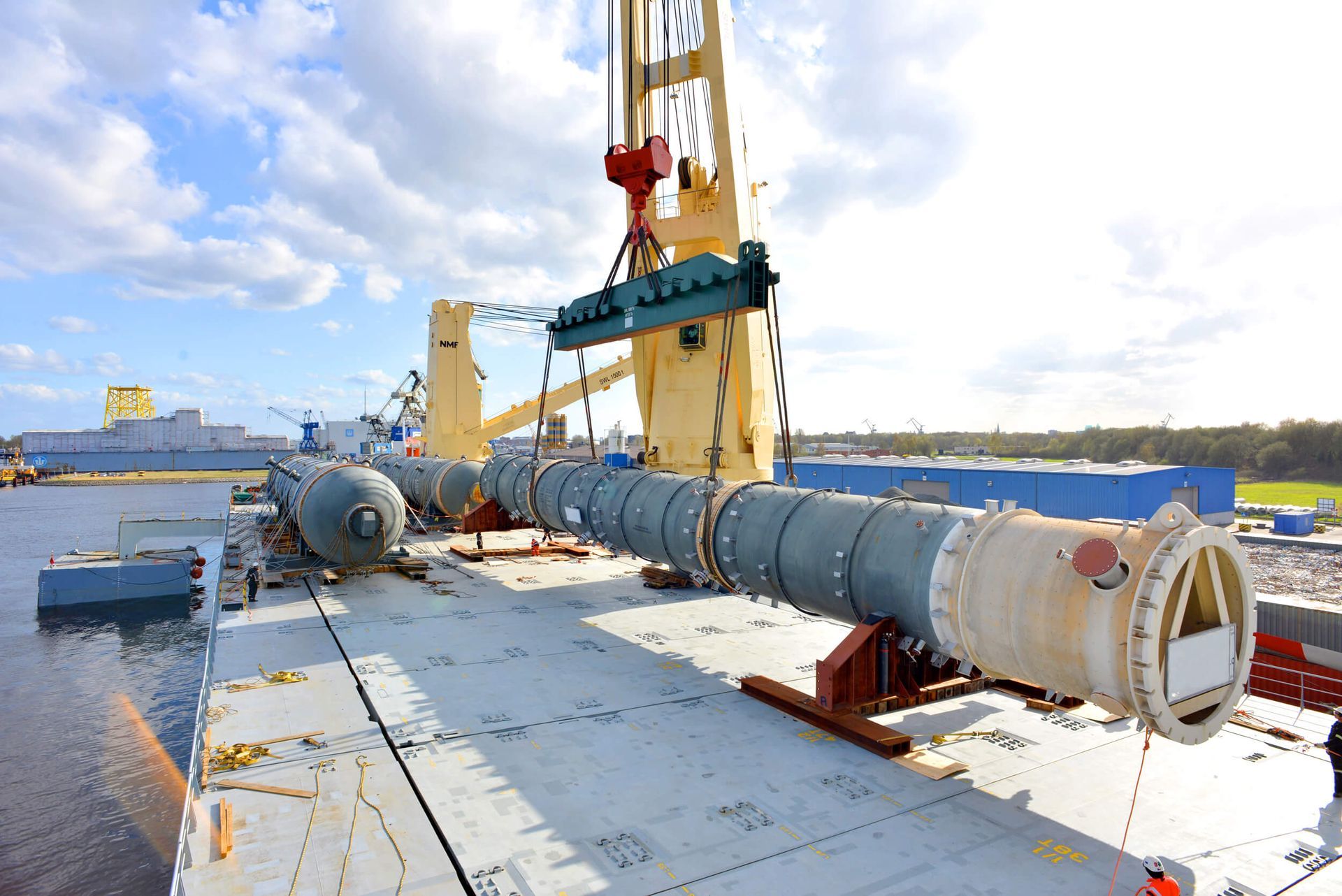 A crane lifts a long, cylindrical industrial component on a ship, likely for transport.
