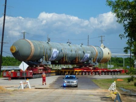 A large, white industrial pipe being lifted by a crane over a truck at a port.