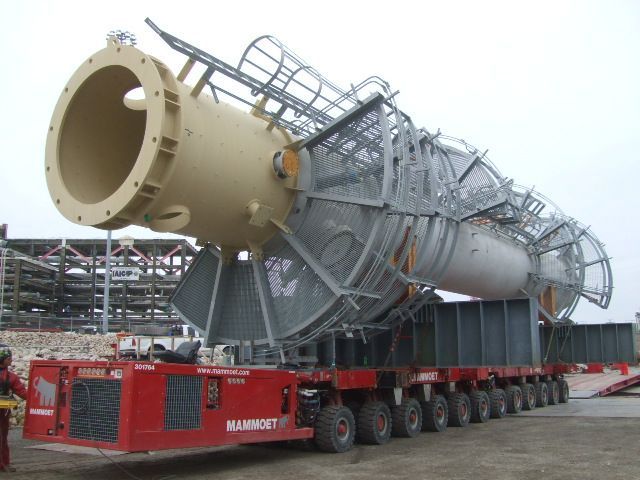 Two large, cylindrical tanks being loaded onto a ship by a crane on a bright, cloudy day.