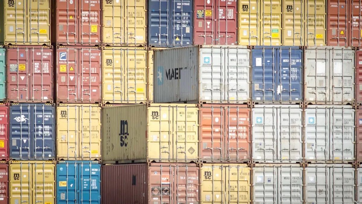 Shipping containers stacked, various colors, at a port.