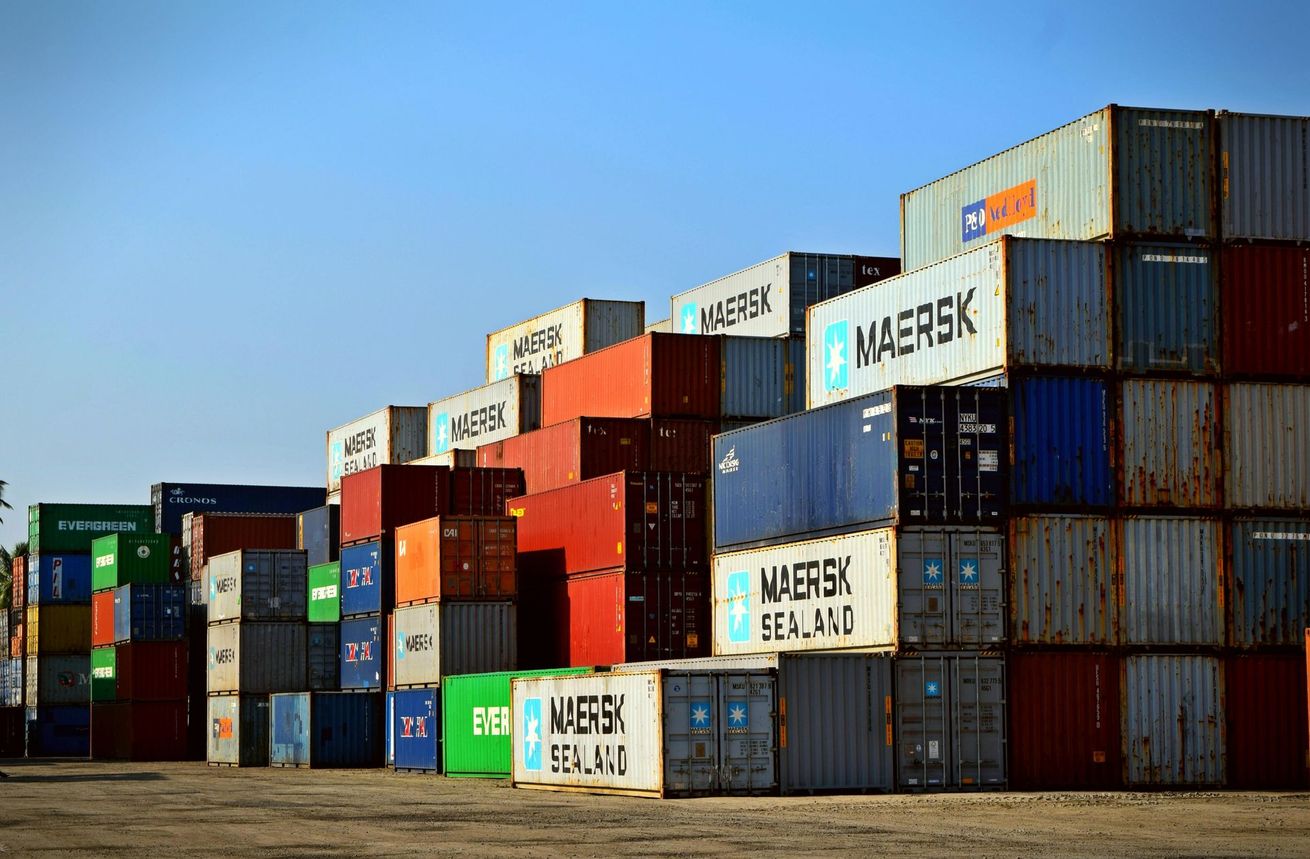 Shipping containers stacked in a port, various colors, under a blue sky.