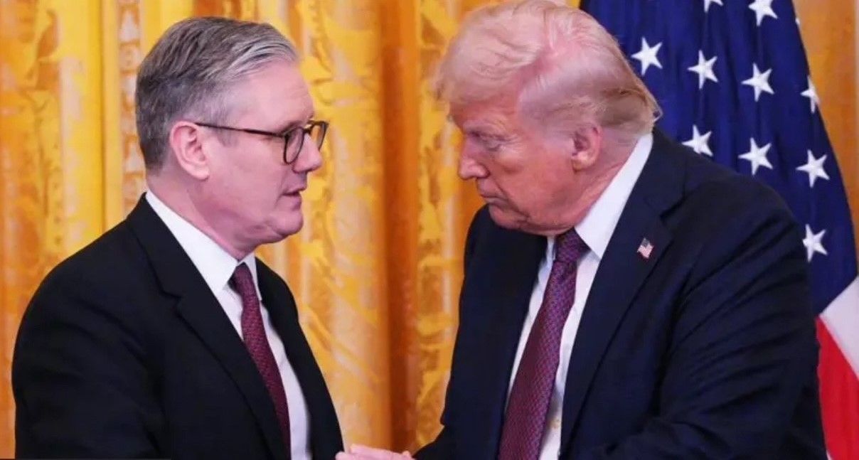 Donald Trump shaking hands with a man in a dark suit; American flag in background.