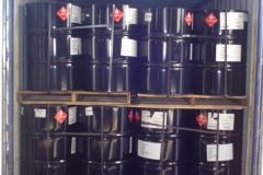 Black drums stacked in a container, labeled with hazard symbols.