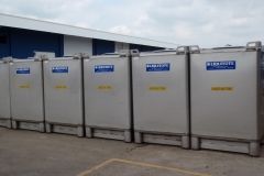 Row of large, silver industrial containers labeled with blue and yellow text outside a warehouse.