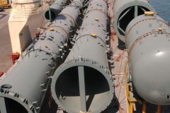 Large gray industrial pipes with open ends, arranged on a ship deck, ready for transport.