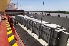 Cargo containers loaded on a ship's deck, ready for transport on a river with a clear sky.