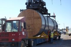 Red truck with large cylindrical object being lifted by crane; workers in vests nearby.