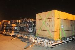 Large wooden crates secured on transport trailers, airport tarmac at night.