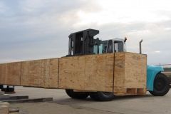Blue forklift carrying long wooden crates.