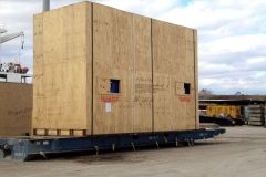 Large wooden crate on a flatbed train car outdoors, in a shipping yard.