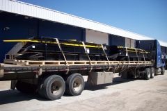 A flatbed truck loaded with black rectangular materials, likely panels, secured with wooden pallets and straps.