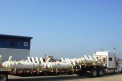 A semi-truck carrying multiple white industrial tanks strapped to a flatbed trailer, parked outside a building.