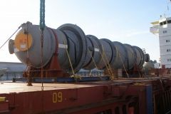 Large cylindrical industrial equipment being lifted onto a cargo ship.