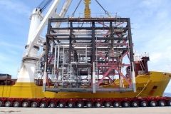 A large crane lifts an industrial structure onto a yellow ship, showcasing transportation of heavy equipment.