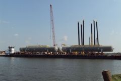 Barge carrying two large, cylindrical industrial tanks with a crane nearby on a waterway.