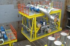 Yellow industrial machinery on a platform with red railings; blue pipes and gray metalwork.