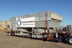 Large industrial unit on a trailer, transported by a semi-truck. The unit is silver and has a logo. Outdoors.