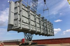 Crane lifting a large, gray industrial container over a body of water.