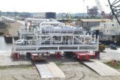 A large white industrial unit on a transport trailer at a dock.