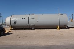 Large, gray cylindrical tank on yellow supports, outdoors, against a clear blue sky.