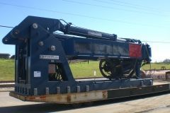 Blue industrial machine on a flatbed trailer, outdoors, on train tracks.