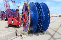 Large blue cable spools with a red crane; two workers nearby. Outdoor, sunny setting.