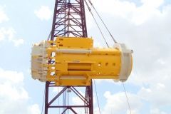 Yellow and white construction equipment suspended by a crane.
