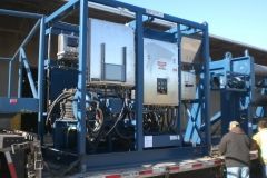 Large blue industrial equipment on a trailer, with metal frame, stainless steel panels, and visible wires.