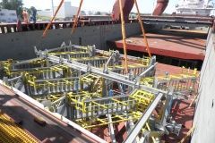 A large metal structure, yellow and gray, is being lifted from a cargo ship by a crane.