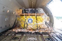 Cargo inside a plane, secured with netting. Yellow objects are visible within the netting.