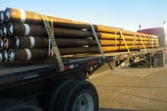 Oil pipes loaded on a flatbed trailer, secured with straps, ready for transport.