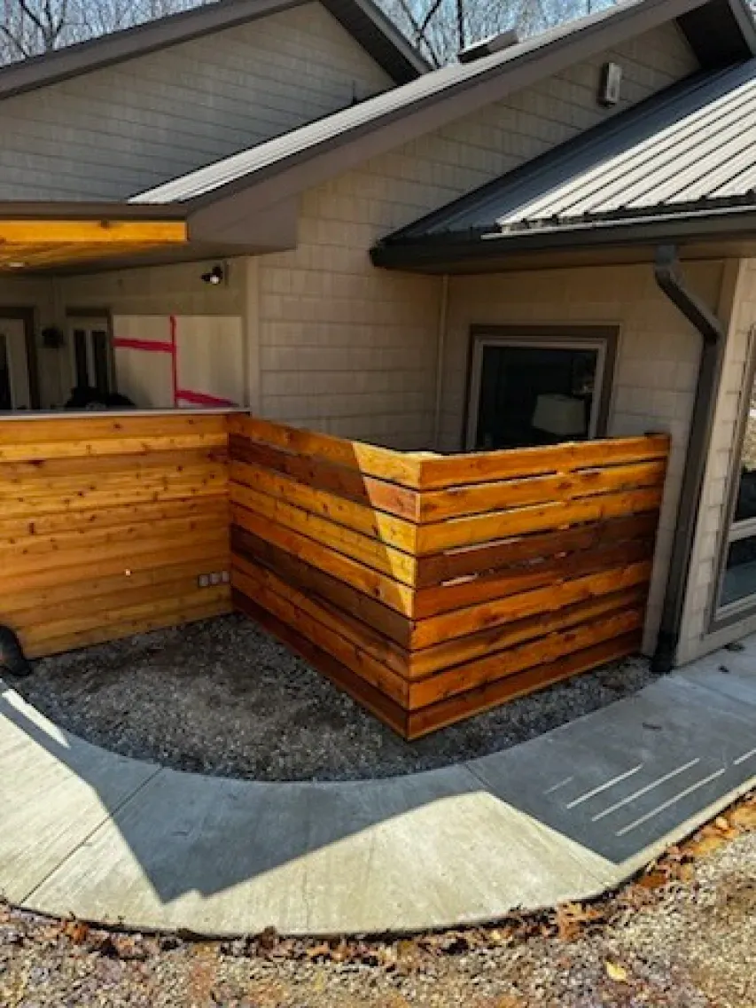 A wooden fence is surrounding a concrete walkway in front of a house.