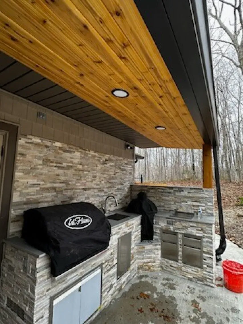 An outdoor kitchen with a grill and a wooden ceiling