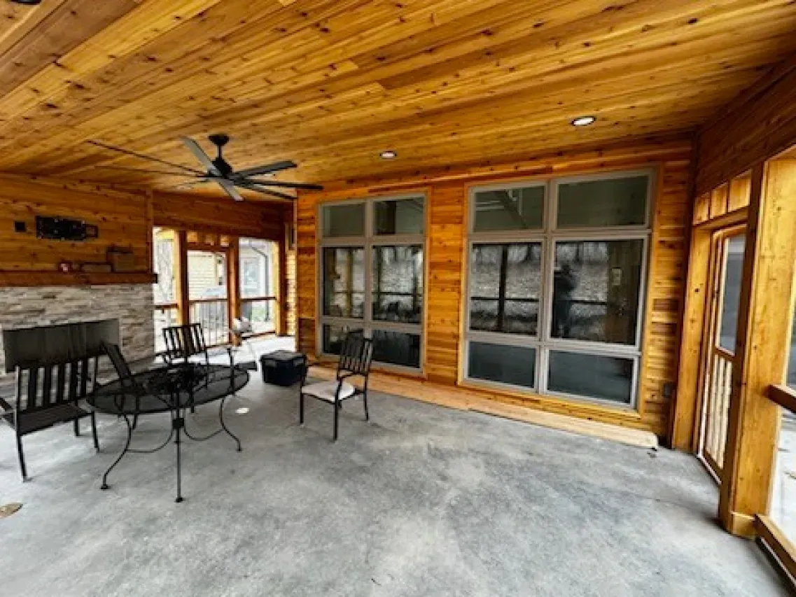 A screened in porch with a table and chairs and a fireplace.