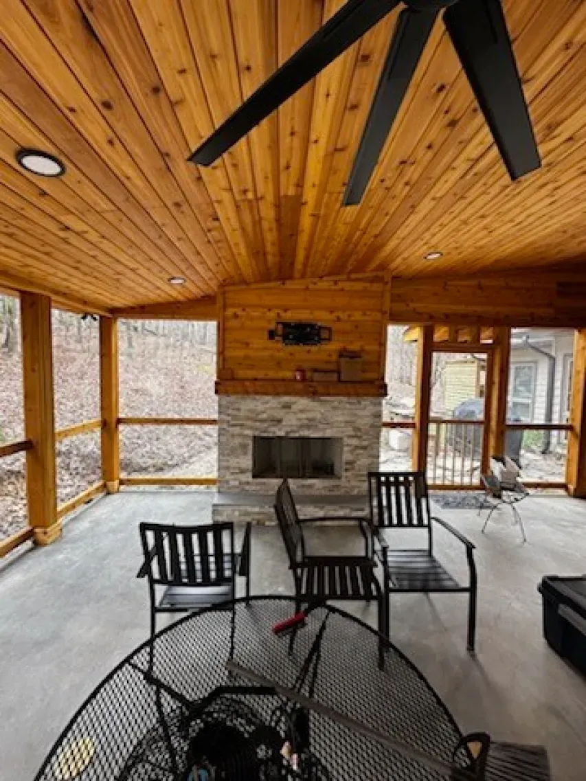 A screened in porch with a fireplace and a ceiling fan