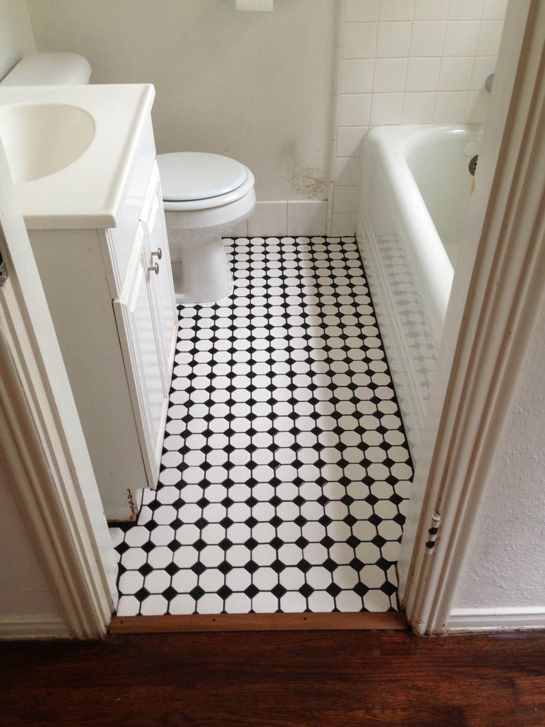 A small bathroom viewed through a doorway, featuring a white vanity, toilet, tub, and black-and-white checkered floor tiles.