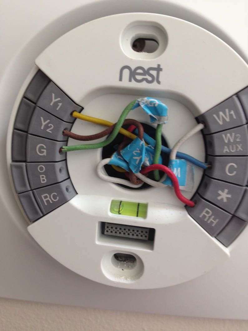 A Nest thermostat base plate mounted on a wall with various colored wires connected to labeled terminals.