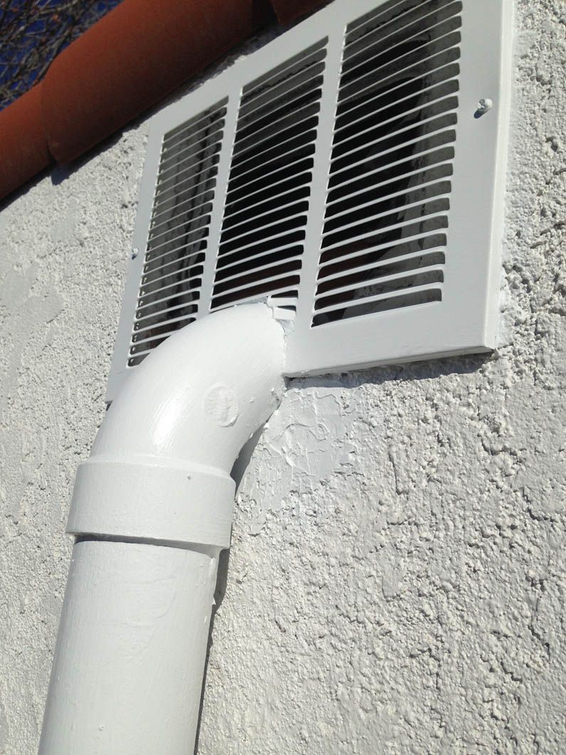 A white PVC pipe elbow connects to a white wall vent on a white stucco exterior wall.