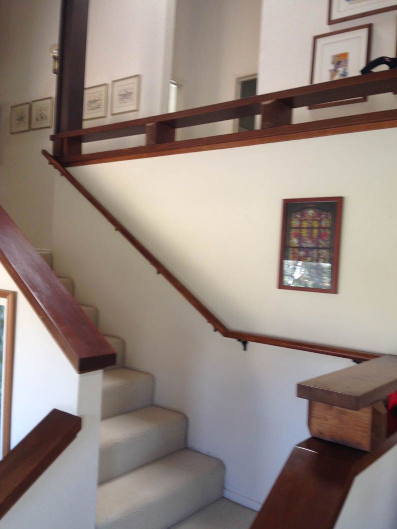 Staircase with cream carpet and dark wood railings, leading up to a landing decorated with framed wall art.