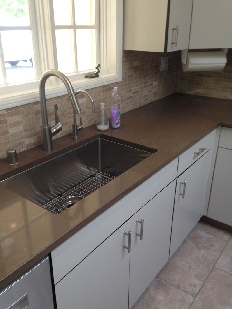 A modern kitchen sink area with a stainless steel faucet, brown countertops, light gray cabinets, and tiled backsplash.