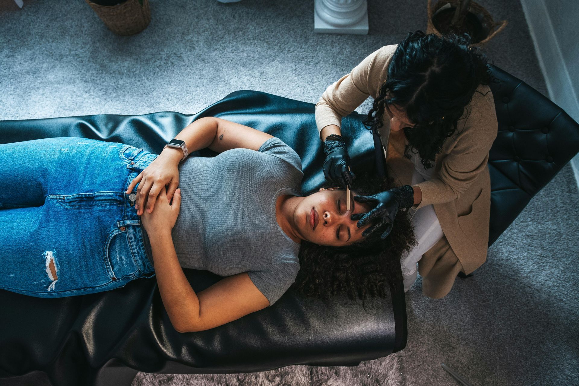 Woman receiving dermaplaning facial; esthetician with gloved hands, black bed.